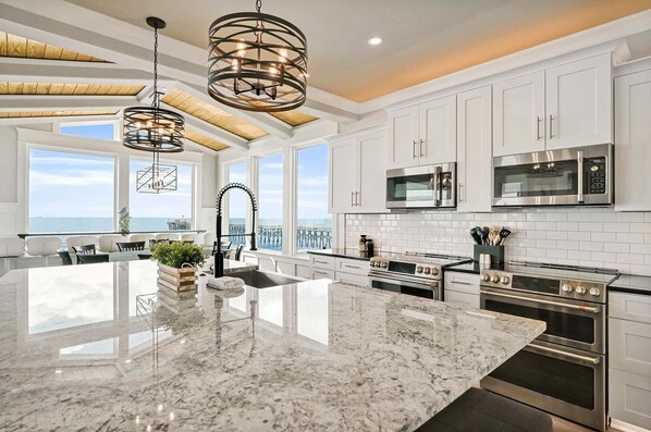 A modern kitchen with a large island, stainless steel appliances, and a view of the ocean.