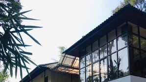 Una casa moderna de dos pisos con amplios ventanales, un automóvil estacionado en la entrada y un muro decorativo de bambú.