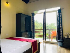 Ein Schlafzimmer mit Bett, Kleiderschrank, einem Balkon mit Vorhängen und Blick ins Grüne.