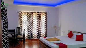 Una habitación de hotel con una cama, una silla, un escritorio y un ventanal con cortinas estampadas.