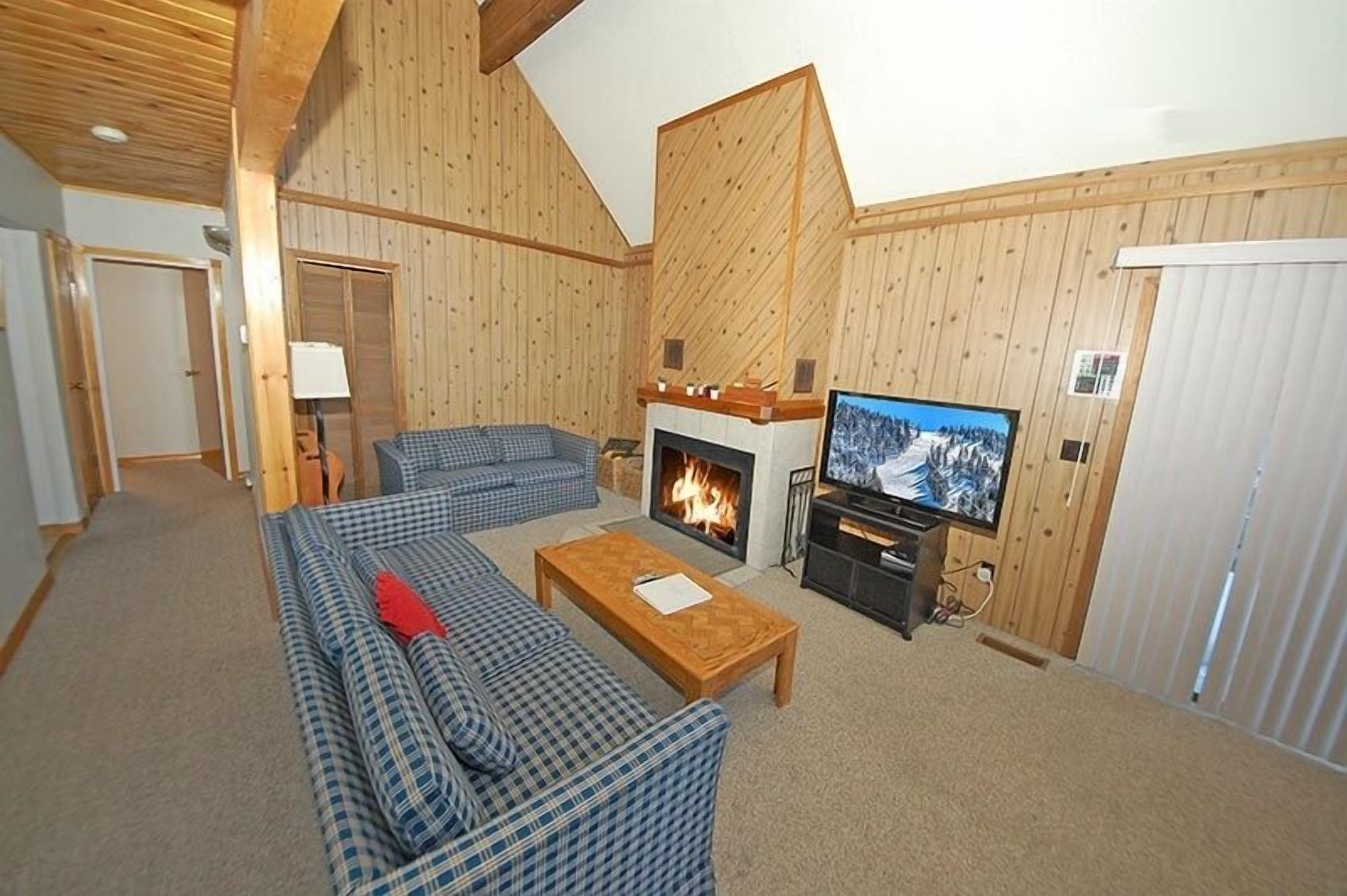 A cozy living room with a fireplace, a television, and a checkered sofa.