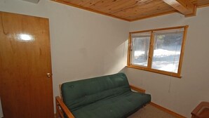 A small room with a green sofa, a wooden door, a window with a view of snow outside, and a wooden ceiling. - 1116 Golden Bear 3 Bedroom Cabin by RedAwning (South Lake Tahoe)