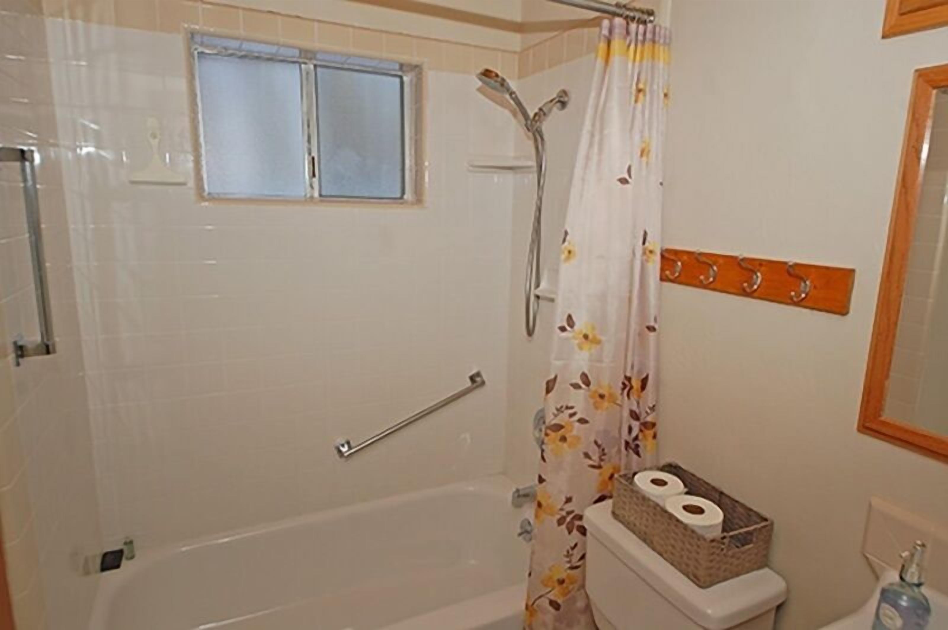 Un baño con bañera, cortina de ducha, ventana, toallero y un inodoro con un cesto de artículos de aseo.
