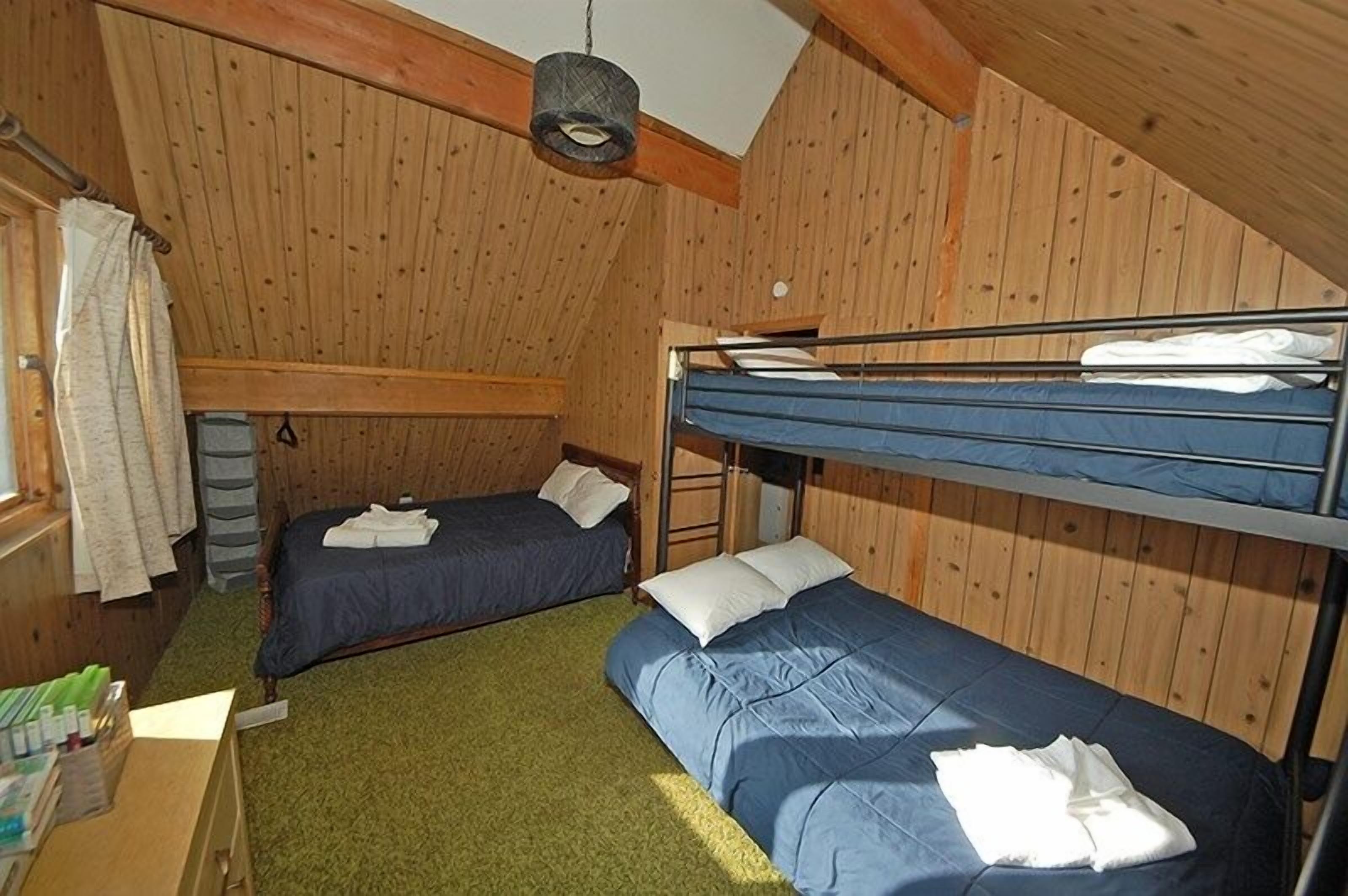 Una habitación pequeña con paneles de madera, con literas y una cama individual.