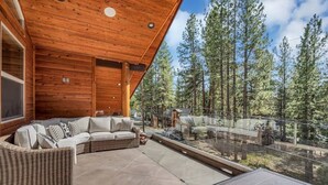 A wooden deck with a sofa and wicker furniture, overlooking a forested area. - 2566 Del Norte 5 Bedroom Home by RedAwning (South Lake Tahoe)