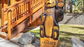 A wooden bear sculpture with "WELCOME" carved on it, positioned in front of a wooden staircase leading to a cabin. - 2566 Del Norte 5 Bedroom Home by RedAwning (South Lake Tahoe)