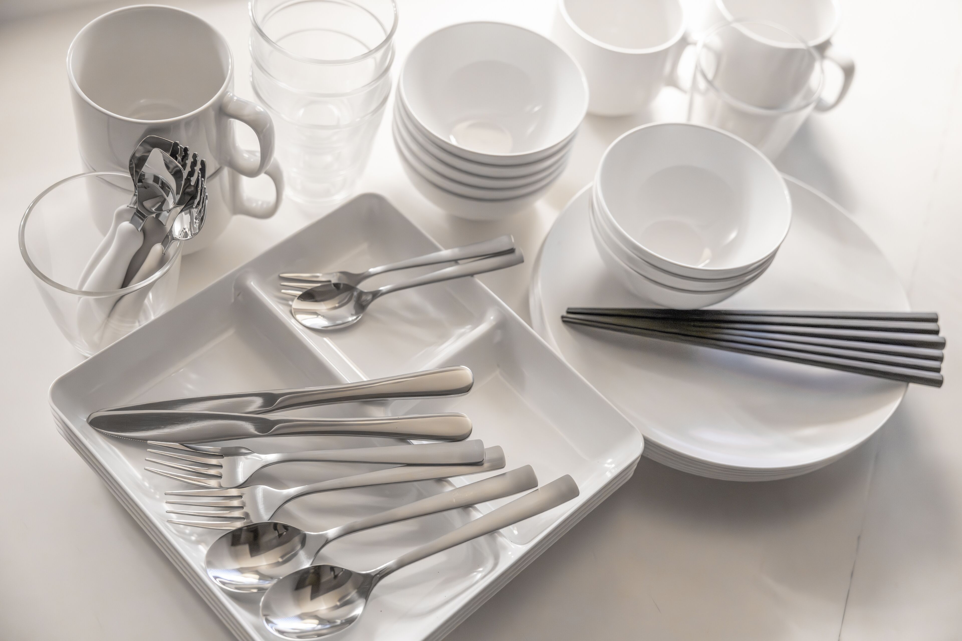 Une table bien dressée, avec des assiettes, des bols, des tasses et des couverts blancs.