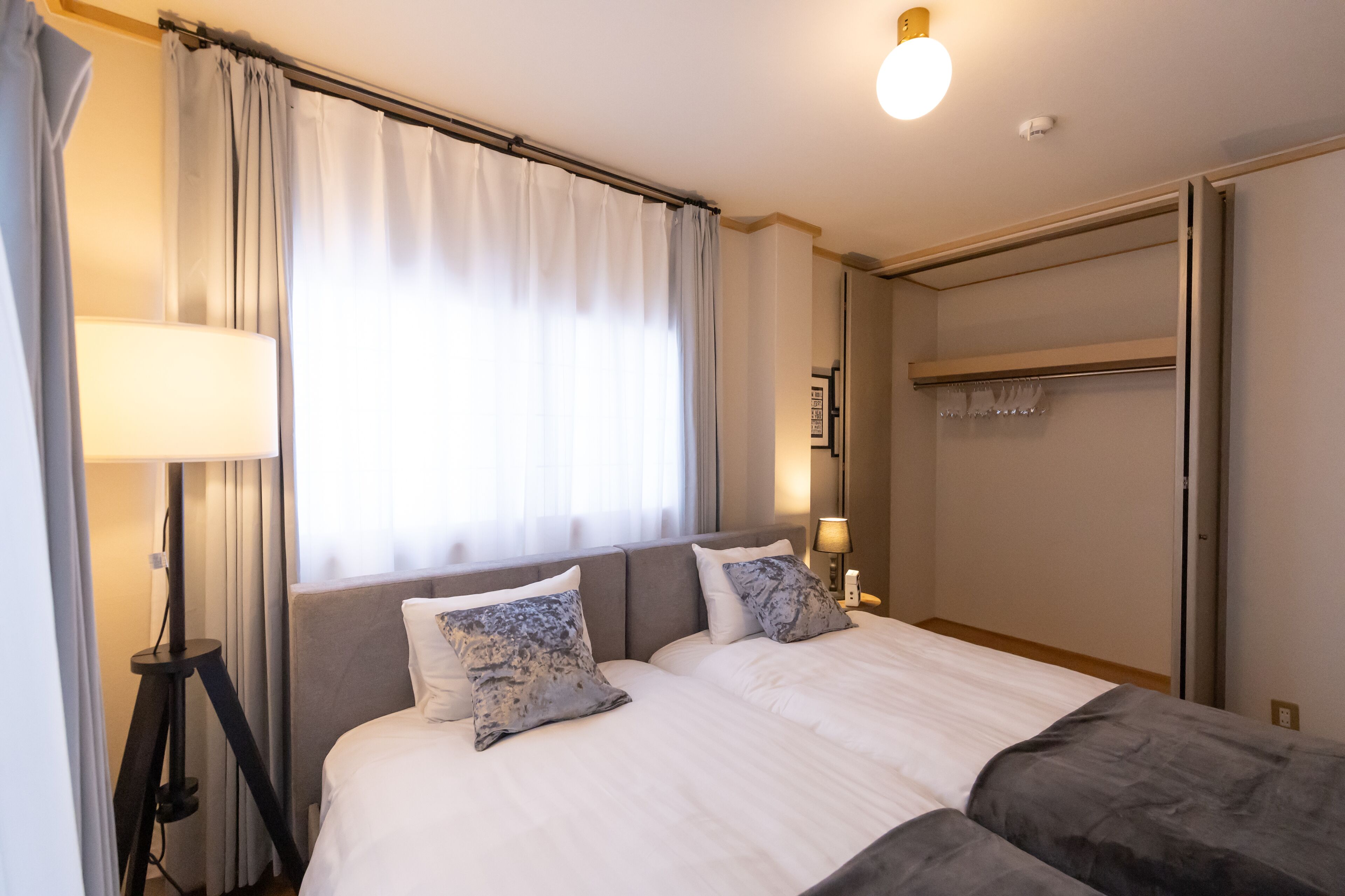Habitació d'hotel amb un llit, una làmpada de nit, un armari i una finestra amb cortines.