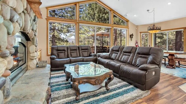 A spacious living room with a stone fireplace, leather sofas, and large windows offering a view of the outdoors.