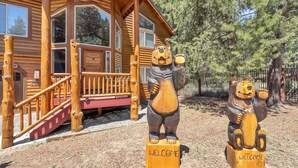 A wooden cabin with large windows and a porch. Two bear statues are placed in front, each with a 'WELCOME' sign.