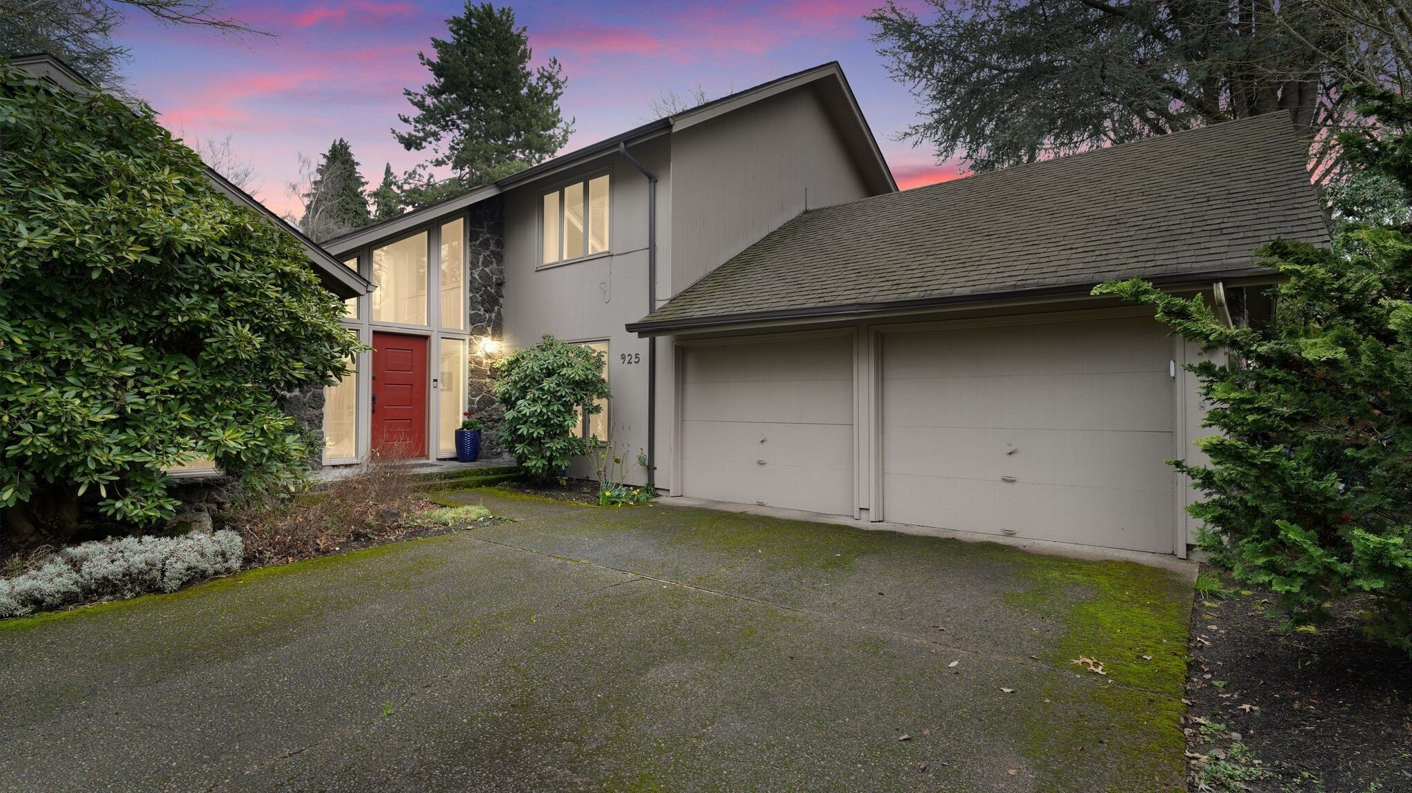 A modern two-story house with a stone facade, a red door, and a garage.