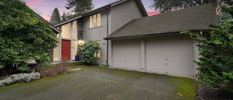A modern two-story house with a stone facade, a red door, and a garage.