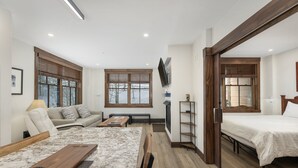 A modern hotel room with a wooden floor, a sofa, a bed, a TV, and a desk.
