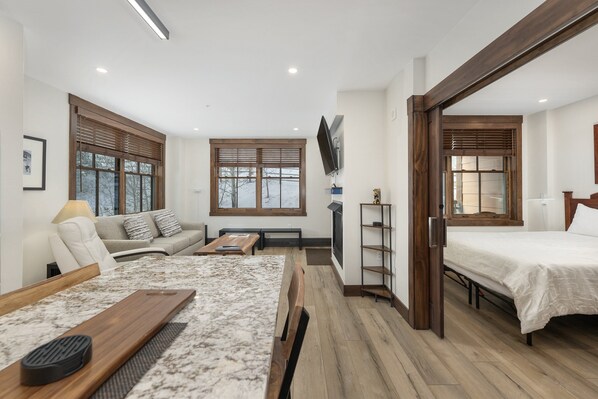 A modern hotel room with a wooden floor, a sofa, a bed, a TV, and a desk.