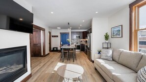A modern living room with a fireplace, a sofa, a dining area, and a kitchen in the background.