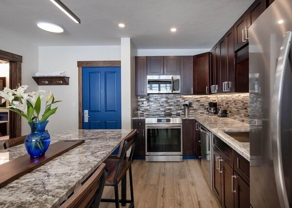 Una cocina moderna con armarios de madera oscura, electrodomésticos de acero inoxidable, una puerta azul y una encimera de mármol.