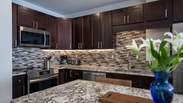 A modern kitchen with dark wood cabinets, a stainless steel microwave, and a tiled backsplash.