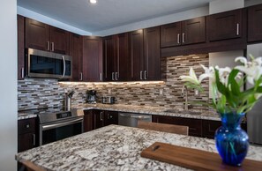 A modern kitchen with dark wood cabinets, a stainless steel microwave, and a tiled backsplash.