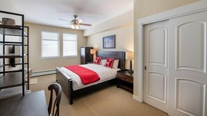 A bedroom with a bed, bedside tables, a desk, a chair, a ceiling fan, and a door. - Select Unit 3606 - Fraser Crossing/founders Pointe 2 Bedroom Condo (Winter Park)