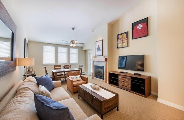 Una sala de estar con sofá, mesa de centro, televisor, chimenea y cuadros en la pared.