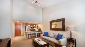 A modern living room with a sofa, coffee table, and a kitchen area in the background. - Select Unit 3606 - Fraser Crossing/founders Pointe 2 Bedroom Condo (Winter Park)