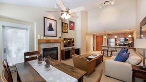 A modern living room with a fireplace, dining table, and seating area. - Select Unit 3606 - Fraser Crossing/founders Pointe 2 Bedroom Condo (Winter Park)