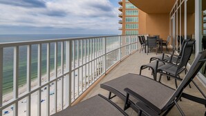 A balcony with a view of the beach and ocean, furnished with lounge chairs and a table.