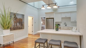 A modern kitchen with white cabinets, a large island with stools, a hanging light fixture, and a potted plant. - Spacious Downtown Hot Springs Vacation Rental! (Hot Springs)