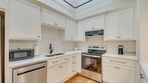 A modern kitchen with white cabinets, a stainless steel dishwasher, a microwave, a sink, a stove, and a coffee maker. - Spacious Downtown Hot Springs Vacation Rental! (Hot Springs)