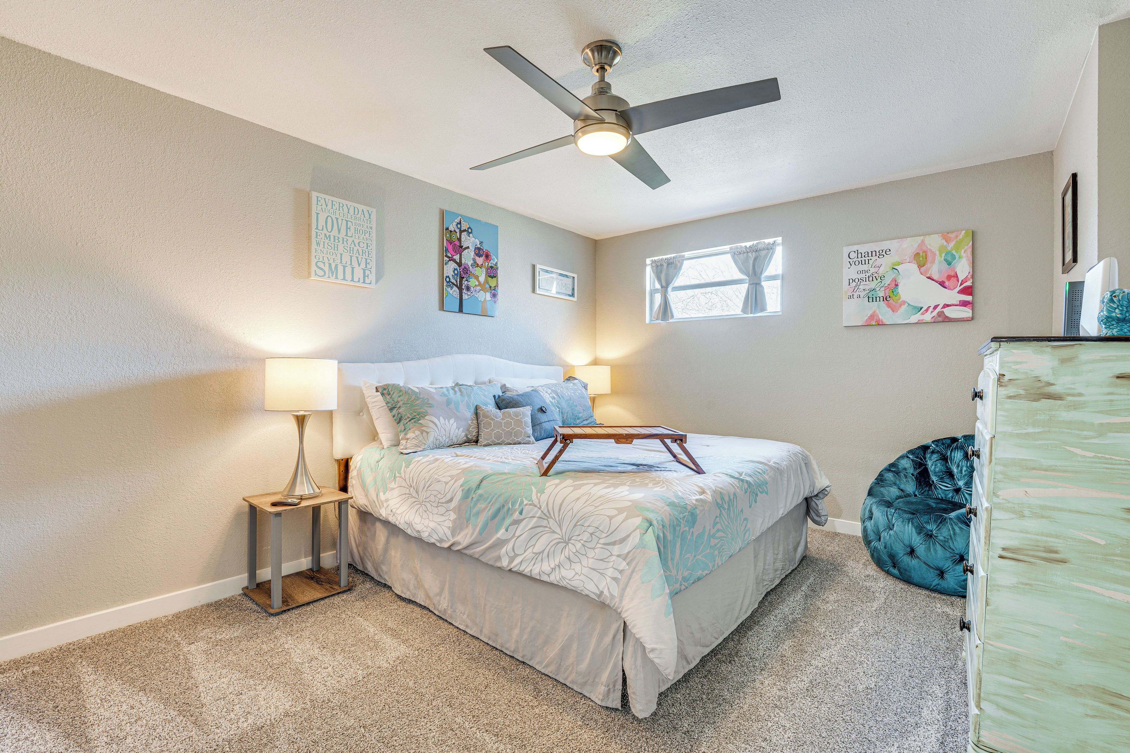A bedroom with a bed, bedside lamps, a ceiling fan, and motivational wall art.
