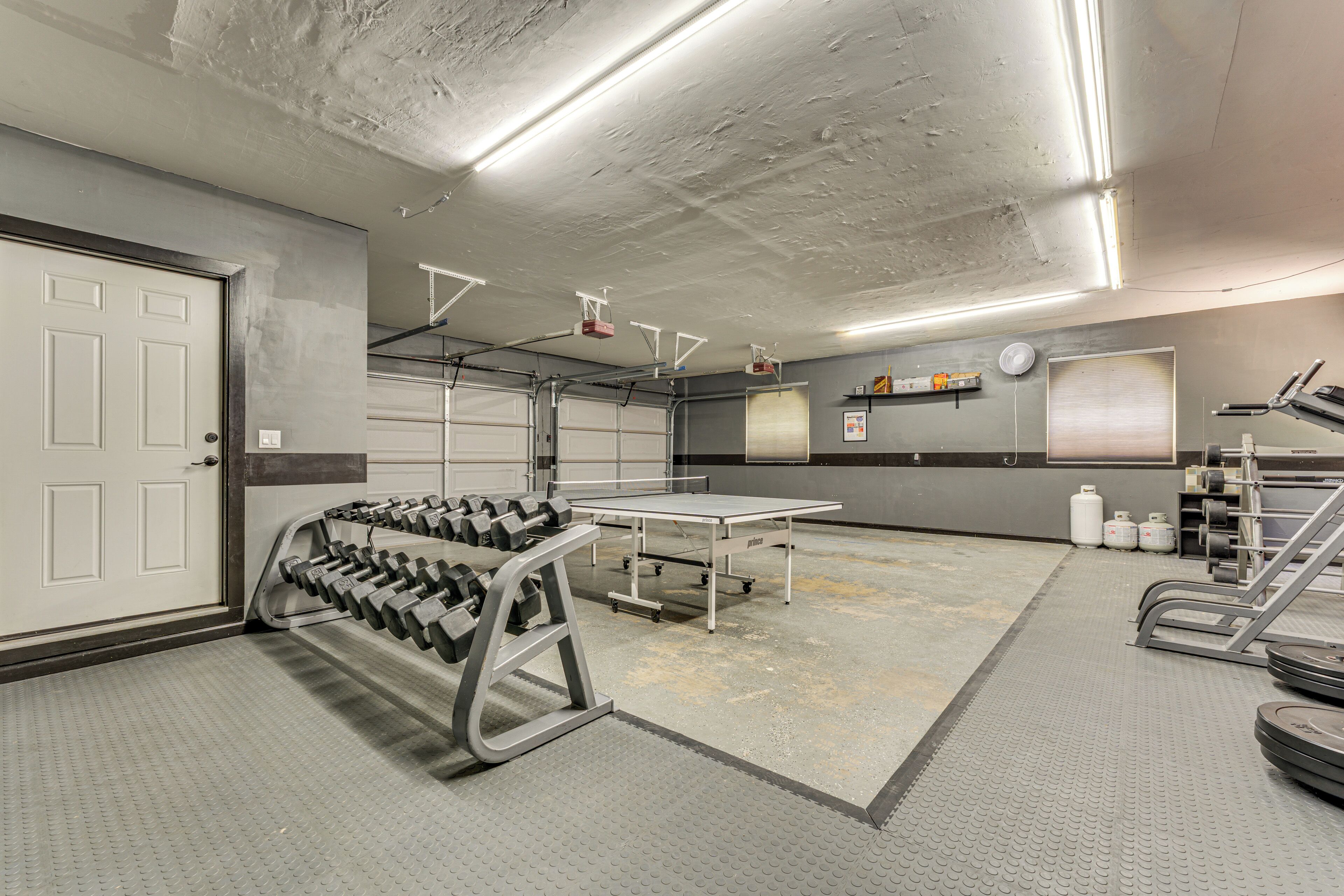 Une salle de sport équipée de matériel de musculation, d’un tapis de course et d’un grand miroir mural.