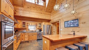 Una cocina amplia con armarios de madera, una isla grande con taburetes, un refrigerador de acero inoxidable y piso de baldosas de piedra.