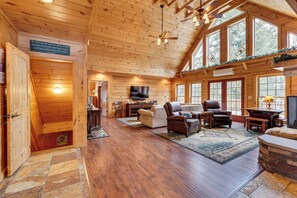 A wooden cabin interior with a dining area, leather sofas, and a fireplace.