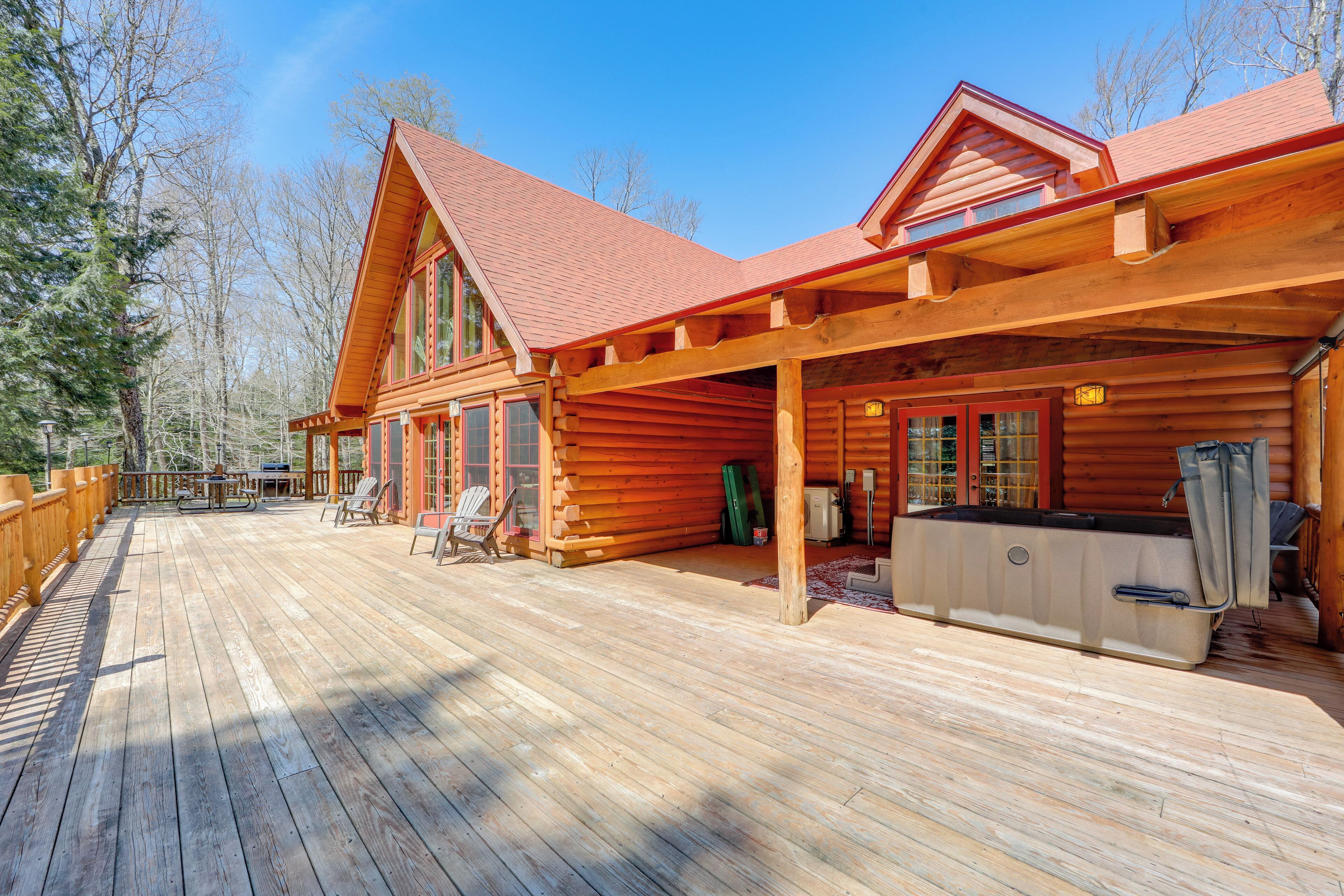 A log cabin with a wooden deck, outdoor seating, and a hot tub.