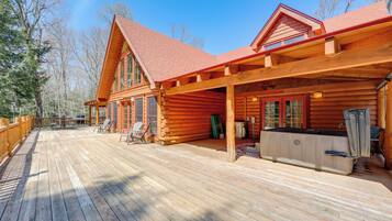 A log cabin with a wooden deck, outdoor seating, and a hot tub.