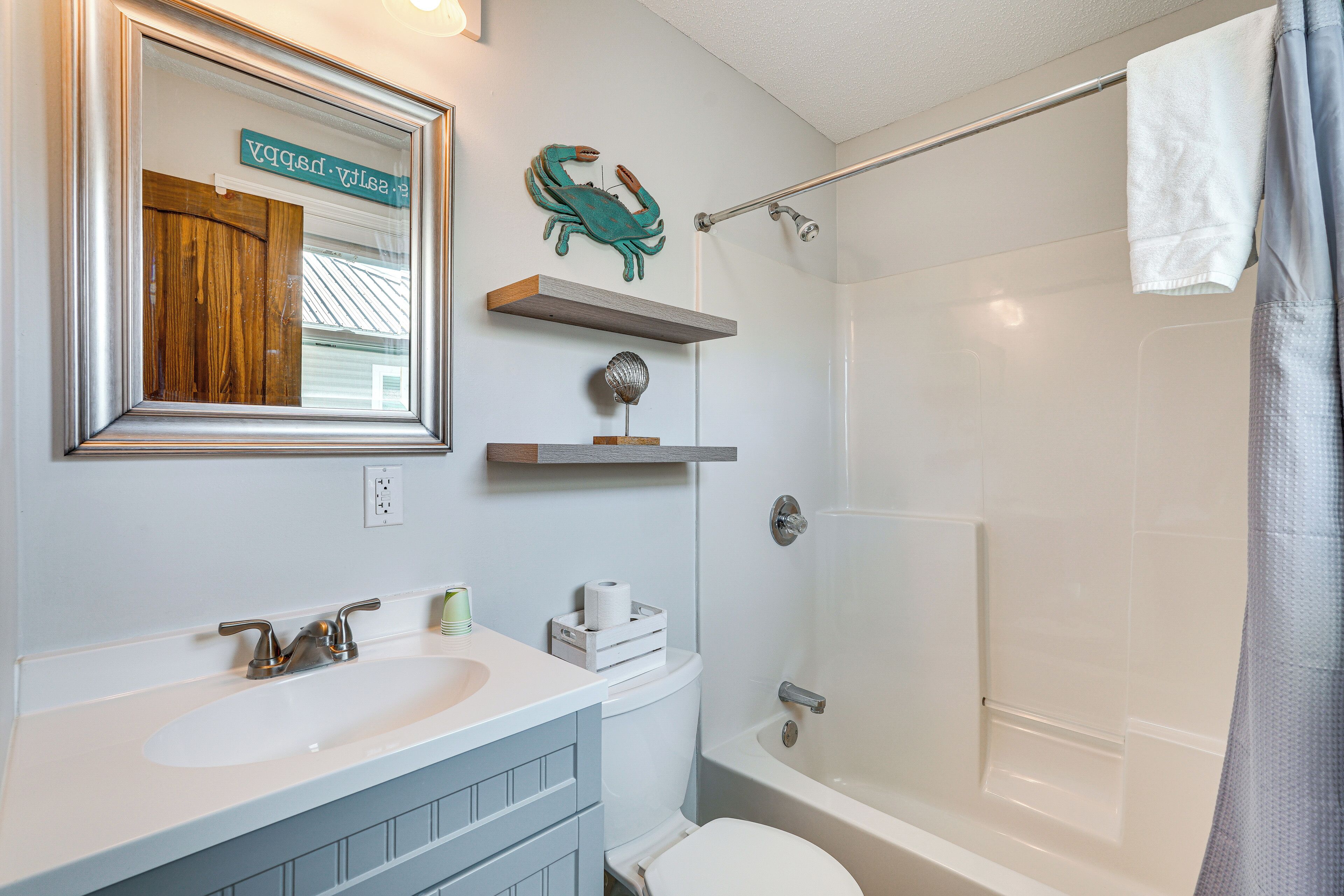 Une salle de bain avec un lavabo, des toilettes et une baignoire. Il y a des étagères au-dessus des toilettes et une serviette est accrochée à la baignoire.