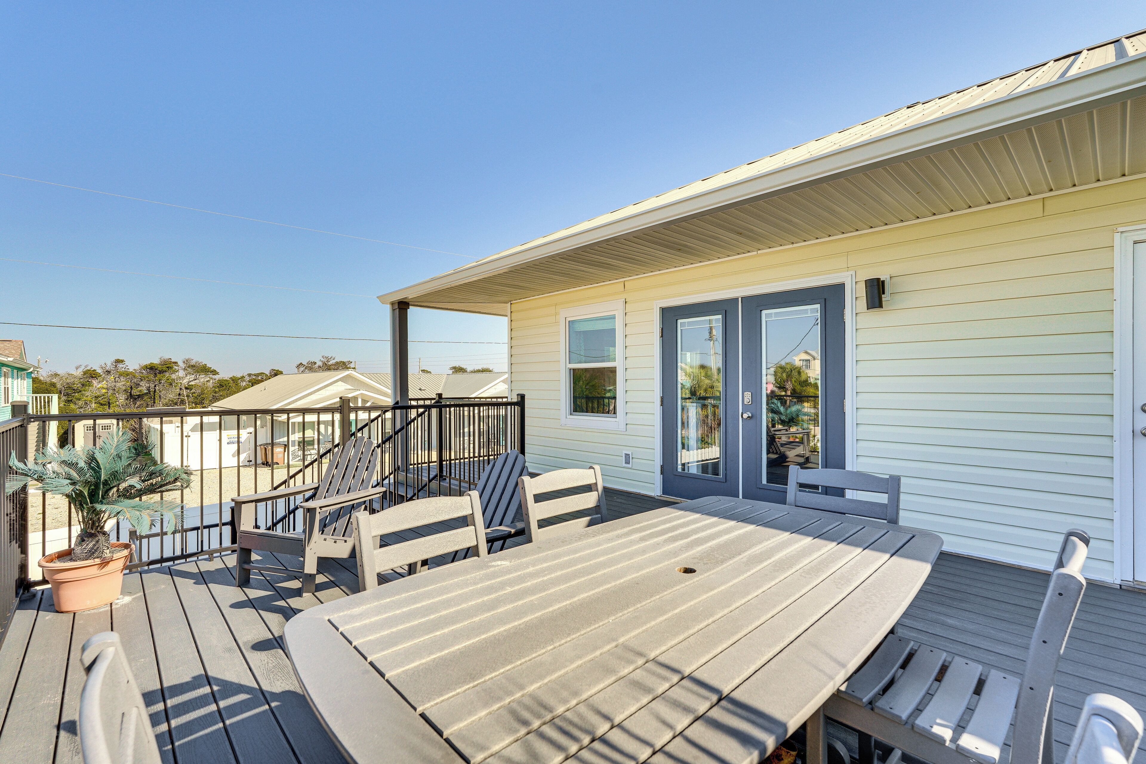 A deck with a table and chairs, a potted plant, and a view of the beach.