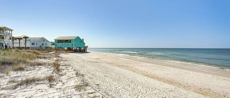 A beach with a turquoise house and white buildings.