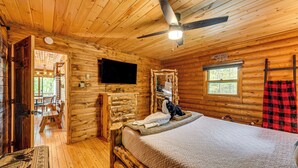 Ein Zimmer in einer Blockhütte mit einem Bett, einem Fernseher, einer Holzkommode und einem Fenster.