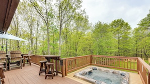 Eine Holzterrasse mit Whirlpool, Gartenmöbeln und Blick auf einen Wald.
