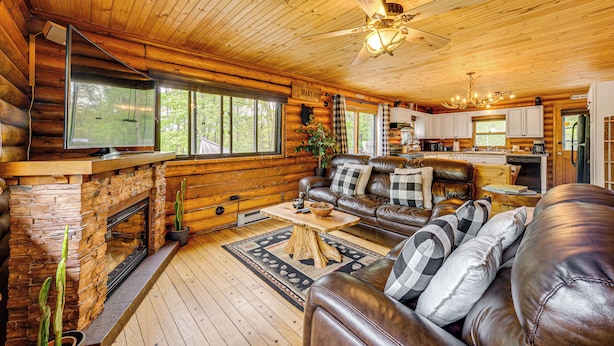 Ein Holzblockhaus-Interieur mit Kamin, Ledersofa, Esstisch und Küchenzeile.