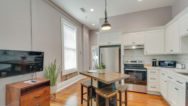 A modern kitchen with white cabinets, a wooden dining table, and a built-in oven. - Downtown Hot Springs Condo - Walk to Restaurants! (Hot Springs)