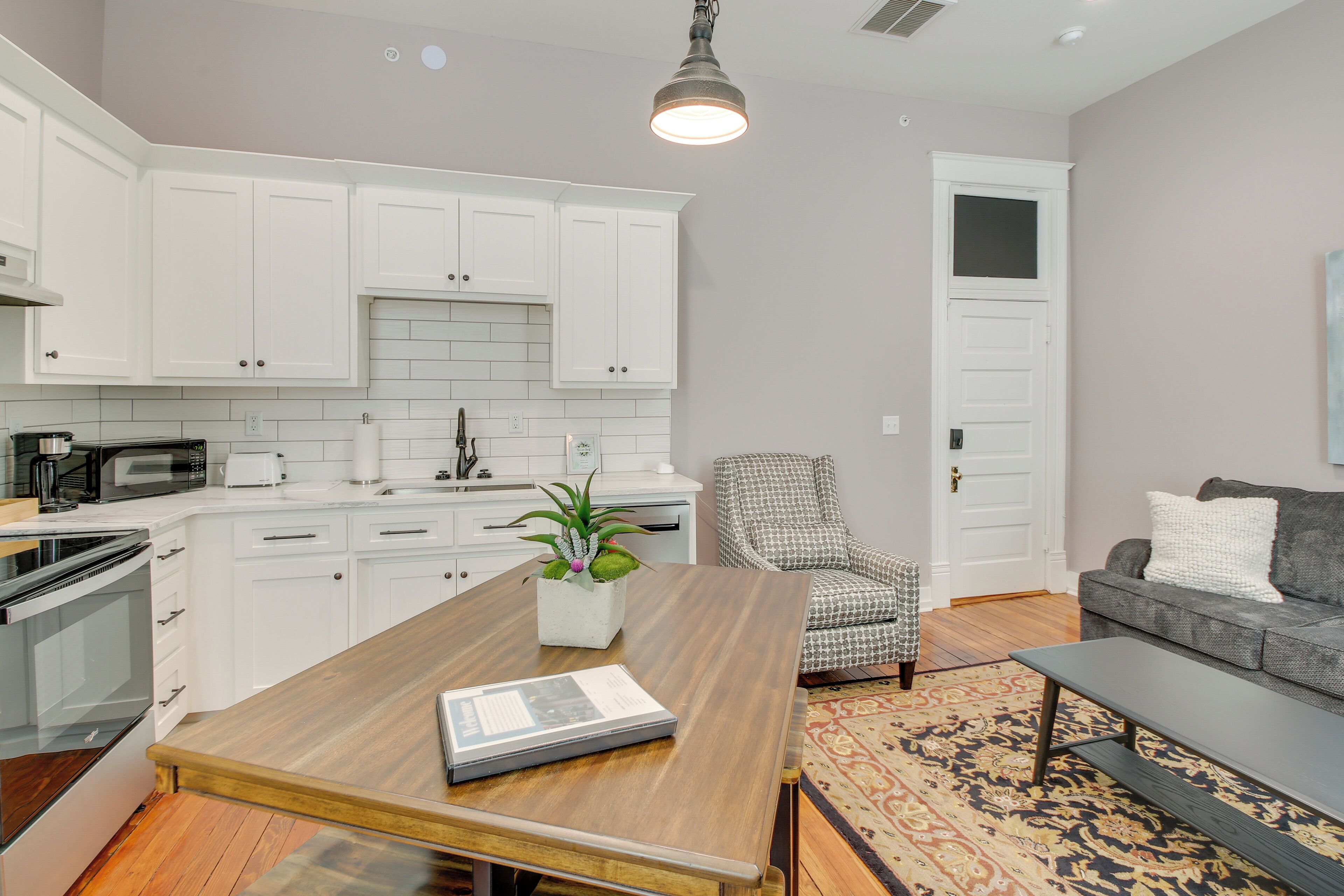 A modern kitchen with white cabinets, a wooden dining table, and a built-in microwave.