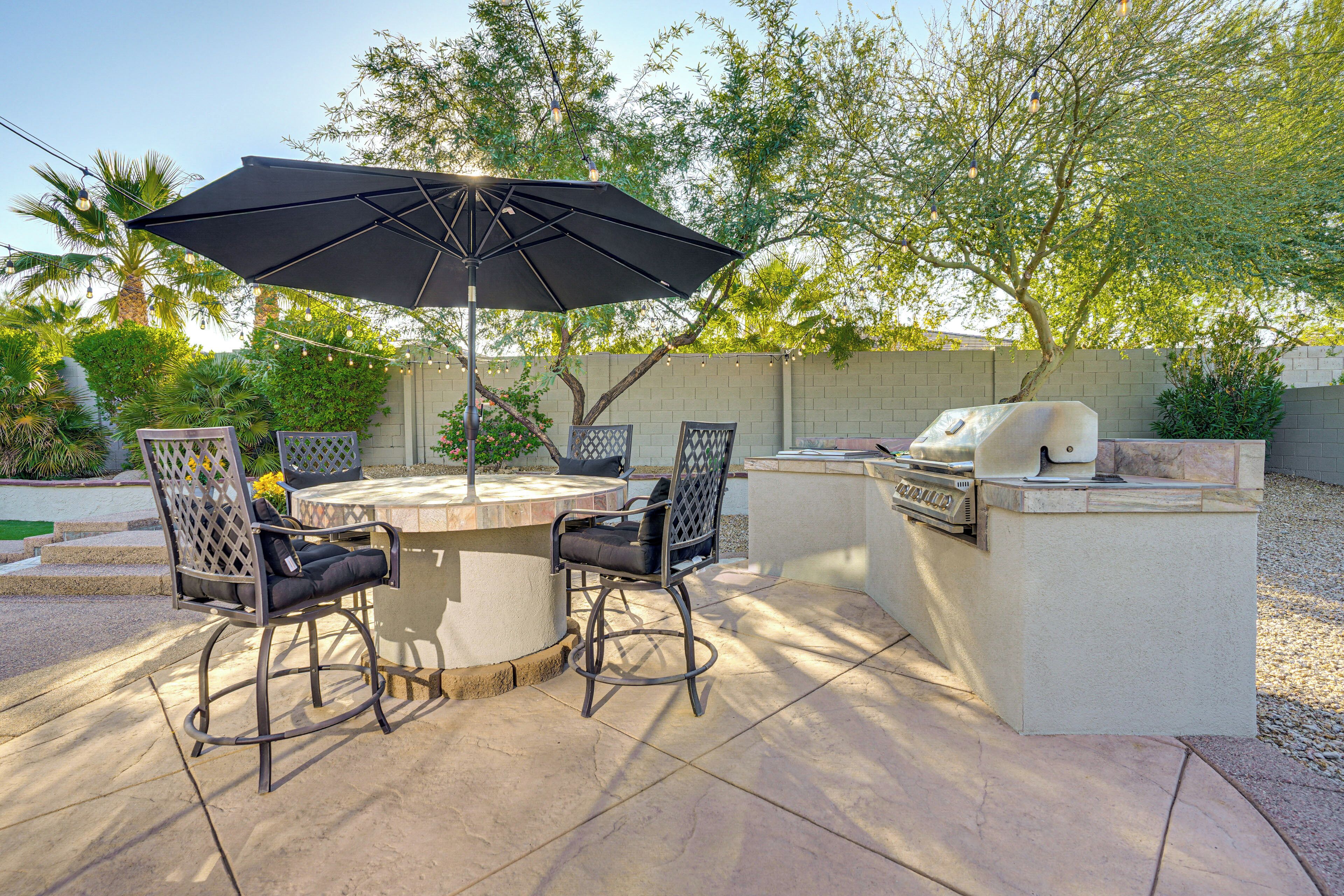 An outdoor patio with a round table, four chairs, a large umbrella, and a built-in grill.
