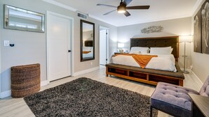 A bedroom with a bed, a ceiling fan, a bedside lamp, a large mirror, and a door. - Bright Tempe Home w/ Fenced Backyard! (Tempe)