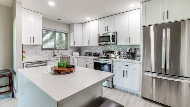 A modern kitchen with white cabinetry, stainless steel appliances, and a central island with a coffee machine and plants. - Bright Tempe Home w/ Fenced Backyard! (Tempe)
