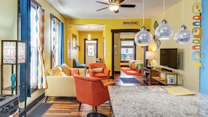 Un salon moderne avec un téléviseur, un fauteuil orange et un ventilateur de plafond.