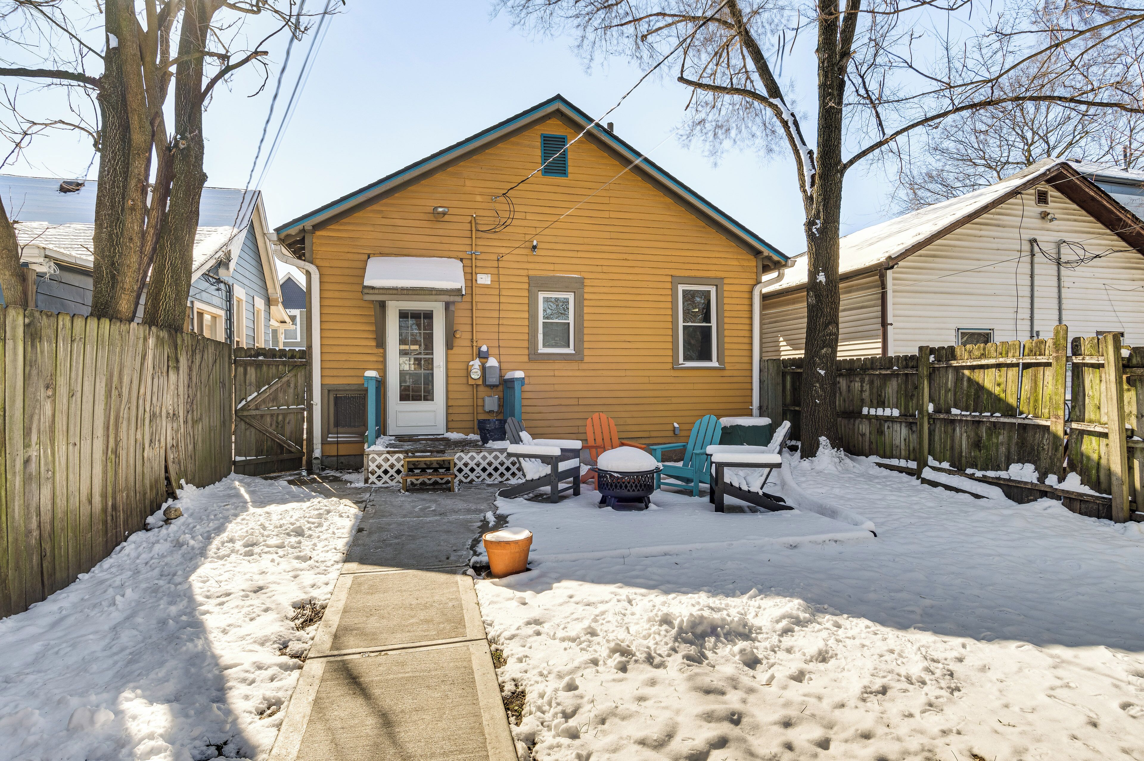A two-story house with a front porch, a wooden fence, and outdoor seating.