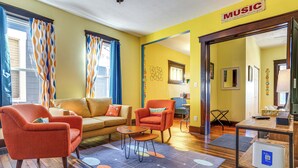Un salon avec un mur jaune, des fauteuils orange, un canapé marron et une table basse.