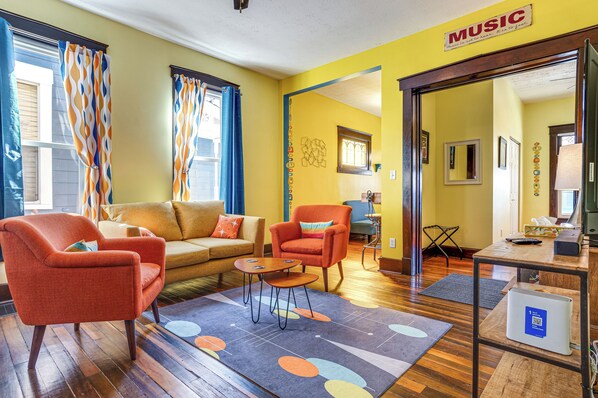 A living room with a yellow wall, orange armchairs, a brown sofa, and a coffee table. - Retro-inspired Indy Home: Walk to Fountain Square! (Indianapolis)